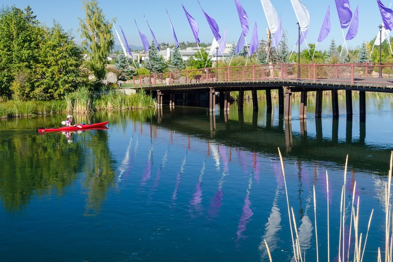 Kayakers paddling the Deschutes River by the footbridge in the Old Mill District