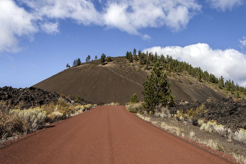 Red cinder road spiraling up Lava Butte between black lava and pines