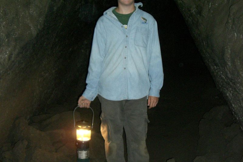 Visitor holding a lantern in the dark lava tube of Lava River Cave