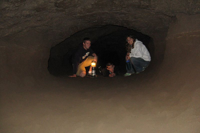 Visitors with a lantern resting in a low section of the Lava River Cave tube