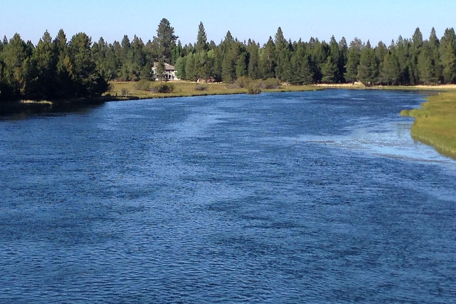 Deep blue Deschutes River flowing past pines and a home in Sunriver