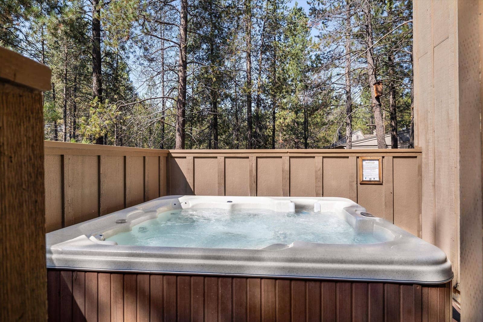 Private hot tub bubbling on the fenced deck, surrounded by tall pines