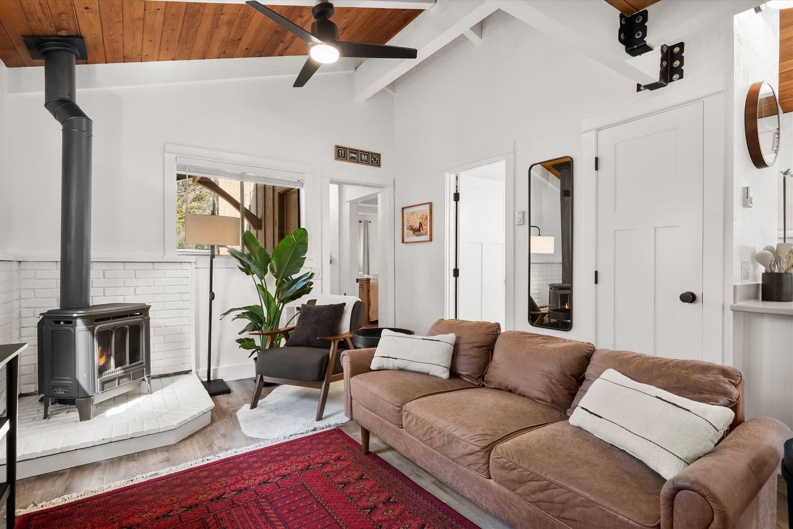 Living room with a wood stove, deep sofa, red patterned rug, and vaulted plank ceiling