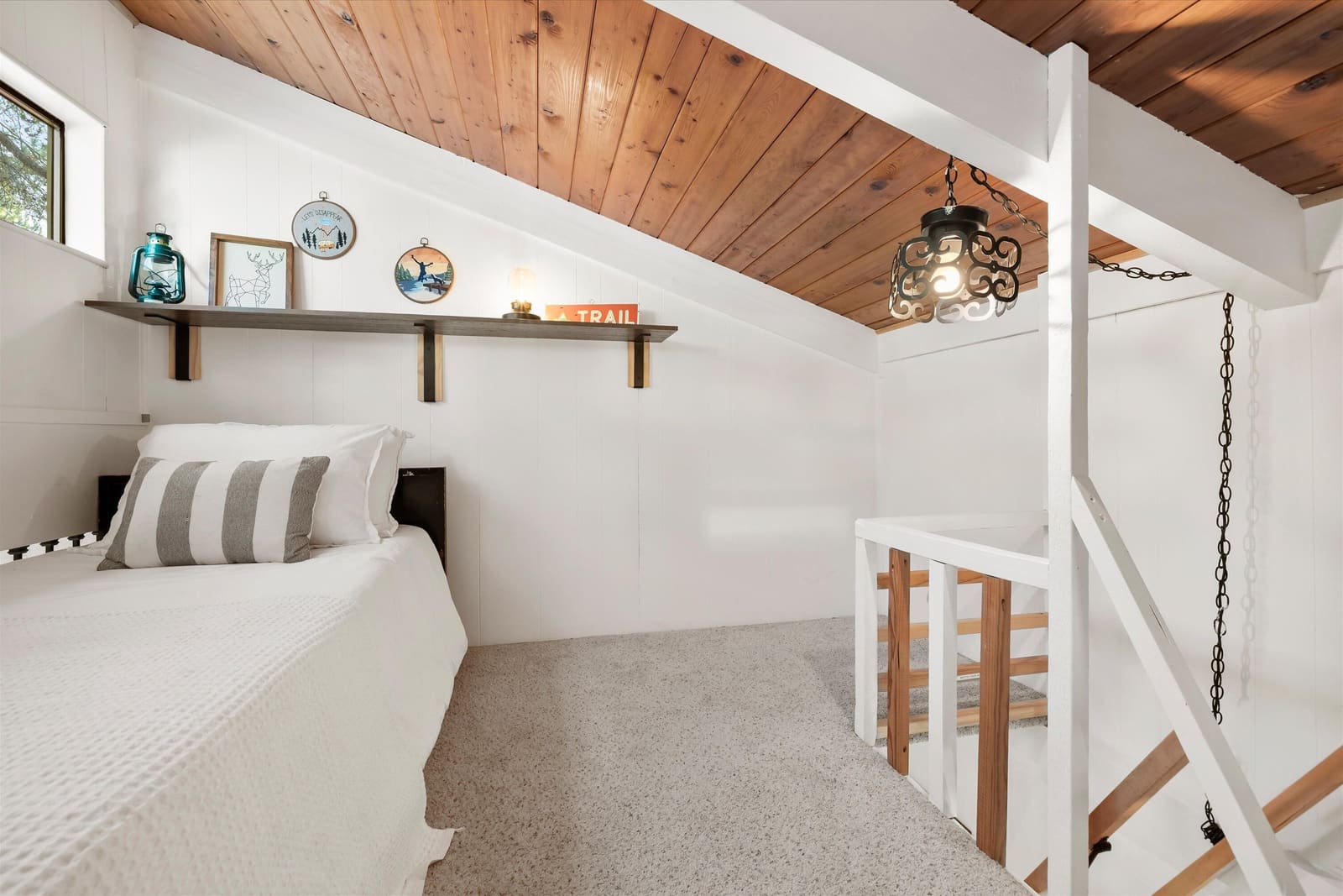 A twin bed in the loft, tucked under the sloped wood ceiling beside the stair railing